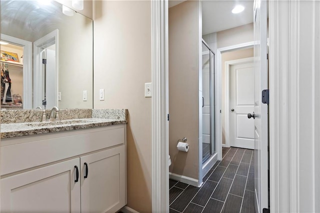 bathroom featuring wood finish floors, a walk in closet, a shower stall, vanity, and baseboards