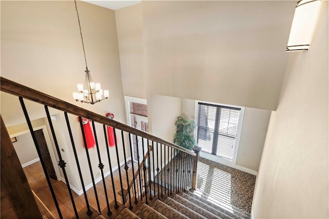 stairs with an inviting chandelier, a high ceiling, baseboards, and wood finished floors