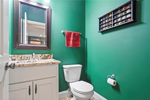 half bath featuring toilet, baseboards, and vanity