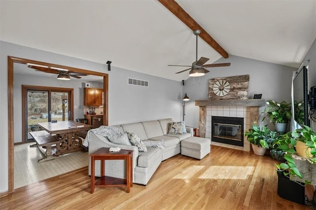 living area with visible vents, a fireplace, lofted ceiling with beams, and ceiling fan