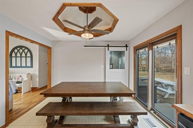 dining space featuring light wood-style floors, a ceiling fan, visible vents, and a barn door