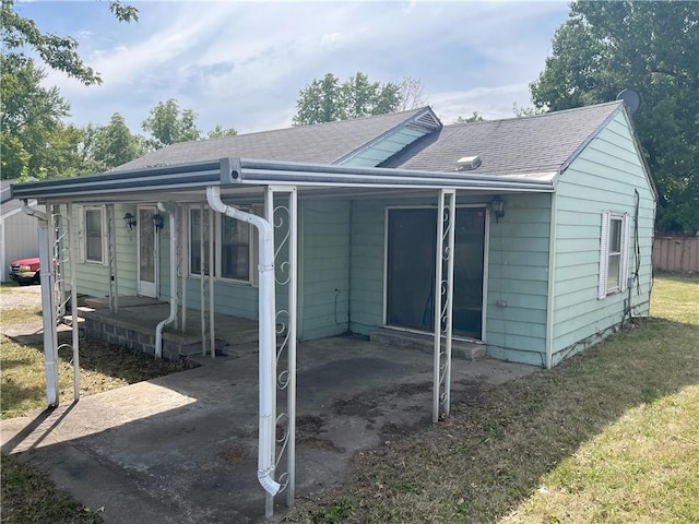 rear view of house featuring covered porch, roof with shingles, and a yard