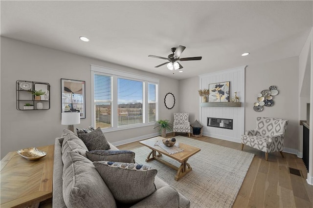 living room featuring recessed lighting, visible vents, a large fireplace, wood finished floors, and baseboards