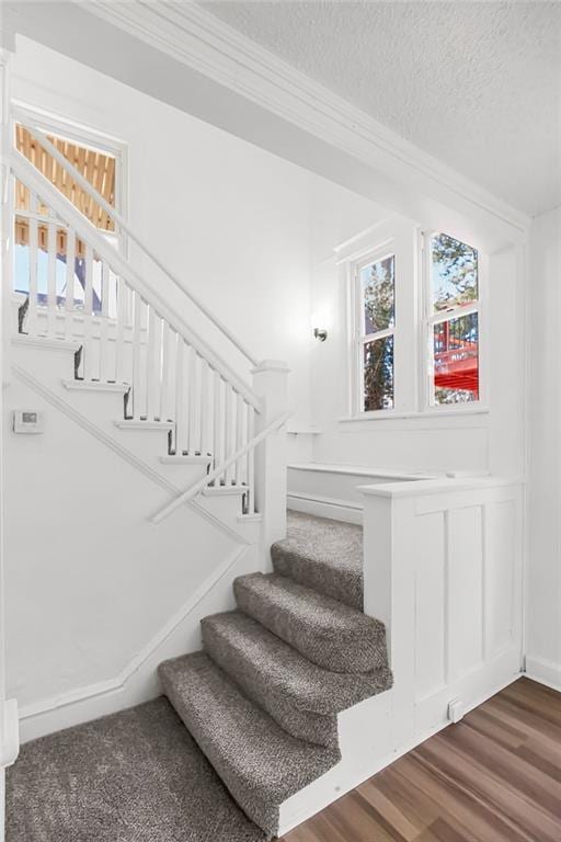 stairs with crown molding, a textured ceiling, and wood finished floors