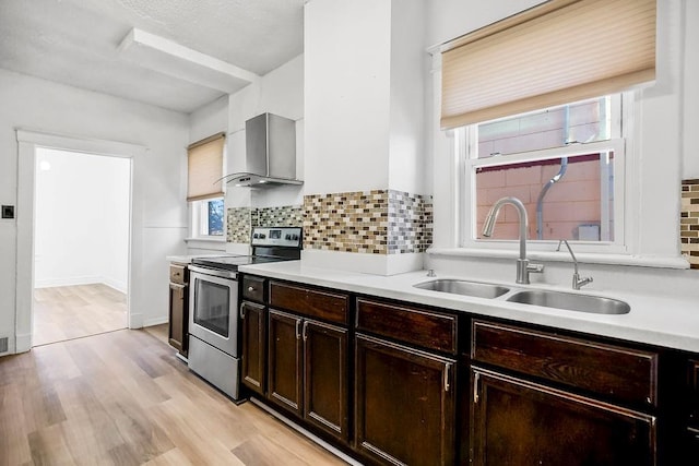 kitchen featuring light countertops, decorative backsplash, stainless steel range with electric cooktop, a sink, and wall chimney exhaust hood