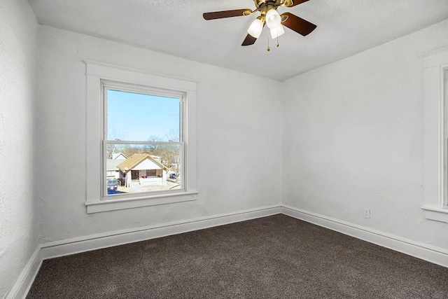 spare room featuring dark colored carpet, ceiling fan, and baseboards