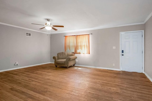 living area with ornamental molding, wood finished floors, visible vents, and baseboards