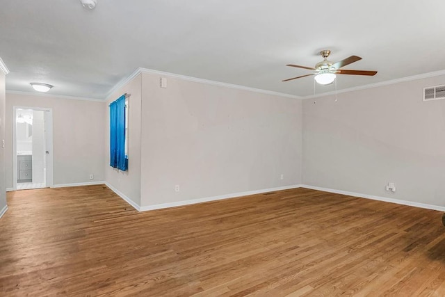 empty room with baseboards, wood finished floors, visible vents, and crown molding