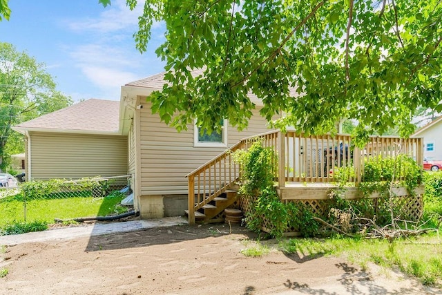 rear view of house featuring a shingled roof, fence, and a wooden deck