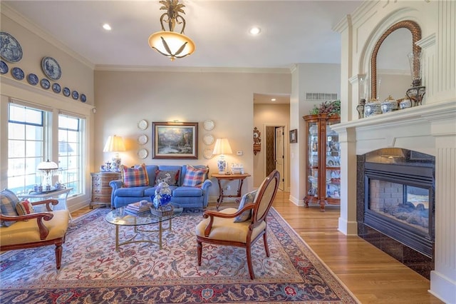 living area with light wood-type flooring, a multi sided fireplace, visible vents, and crown molding