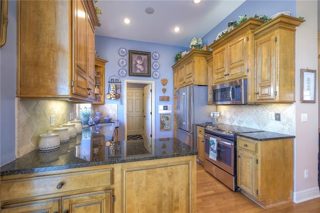 kitchen with a peninsula, light wood-style floors, dark stone counters, and stainless steel appliances