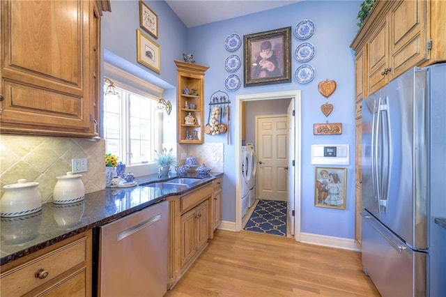 kitchen featuring light wood-style flooring, a sink, appliances with stainless steel finishes, decorative backsplash, and washing machine and clothes dryer