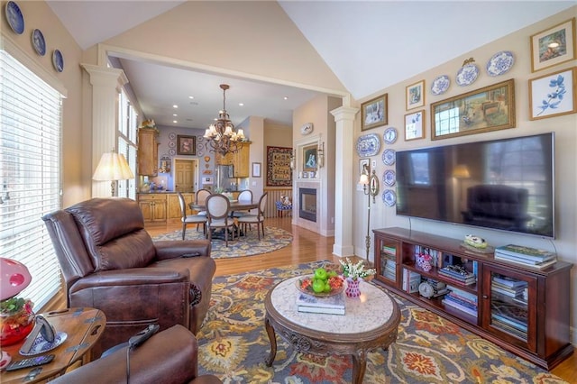 living area featuring lofted ceiling, ornate columns, a notable chandelier, and wood finished floors