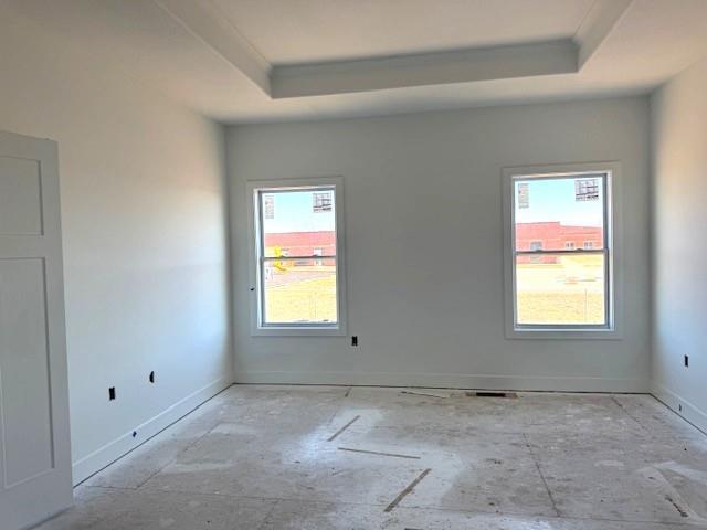 empty room featuring a tray ceiling, crown molding, and baseboards