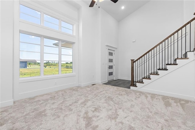 unfurnished living room featuring a towering ceiling, carpet, and stairway