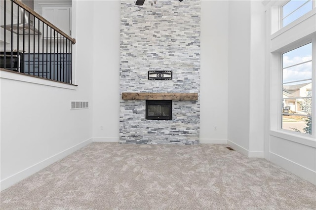 unfurnished living room featuring carpet floors, plenty of natural light, a towering ceiling, and visible vents