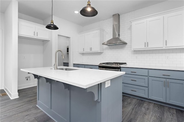 kitchen with tasteful backsplash, white cabinetry, a sink, wall chimney range hood, and stainless steel gas range