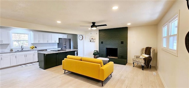 living room featuring light wood finished floors, baseboards, a ceiling fan, a fireplace, and recessed lighting