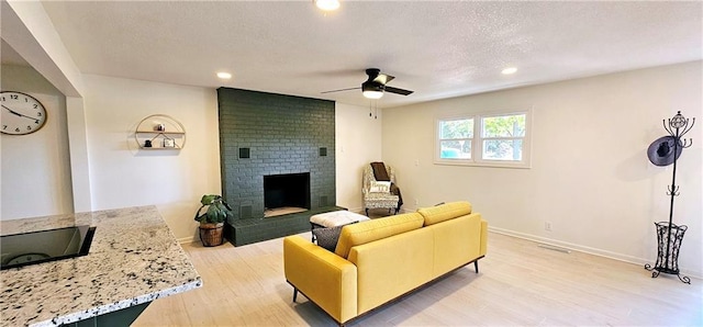 living room with light wood finished floors, a fireplace, baseboards, and a ceiling fan