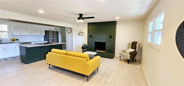 living area with baseboards, a ceiling fan, light wood-type flooring, a fireplace, and recessed lighting