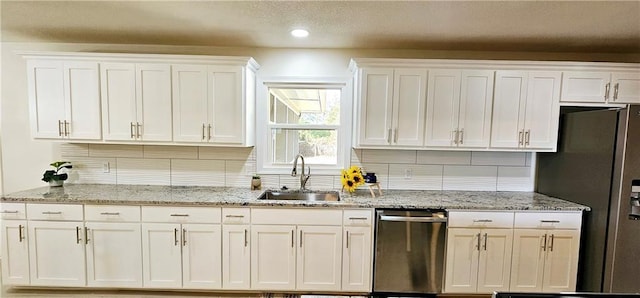 kitchen with appliances with stainless steel finishes, a sink, white cabinetry, and tasteful backsplash