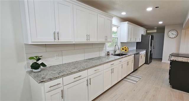kitchen with light wood finished floors, a sink, stainless steel appliances, white cabinetry, and backsplash