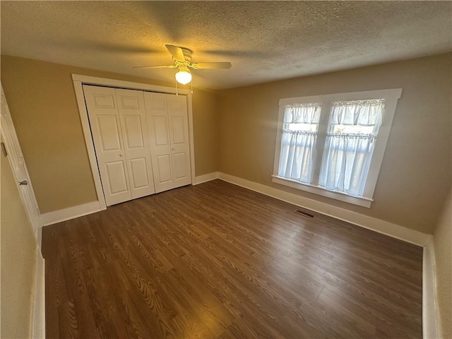 unfurnished bedroom featuring visible vents, baseboards, a textured ceiling, and dark wood finished floors