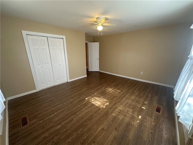 unfurnished bedroom with a closet, visible vents, dark wood-type flooring, and baseboards