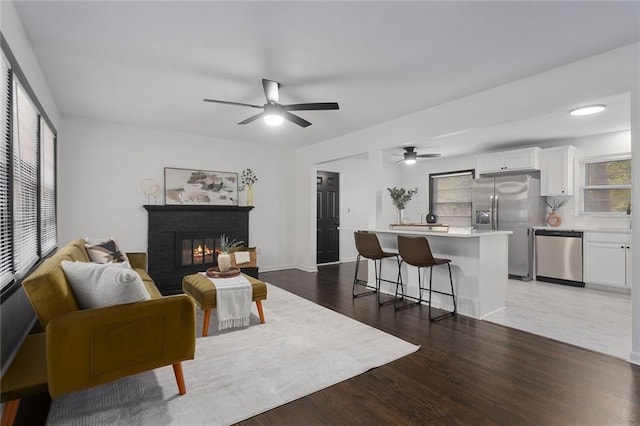 living area with a brick fireplace, baseboards, a ceiling fan, and wood finished floors