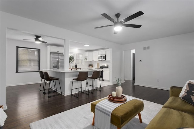 living room with dark wood-style floors, visible vents, ceiling fan, and baseboards