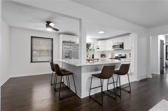 kitchen featuring stainless steel appliances, white cabinets, light countertops, dark wood-style floors, and a kitchen bar