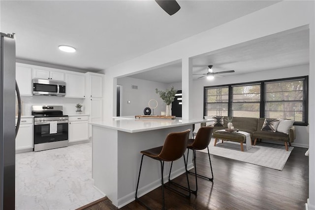 kitchen featuring marble finish floor, stainless steel appliances, light countertops, white cabinetry, and a kitchen breakfast bar