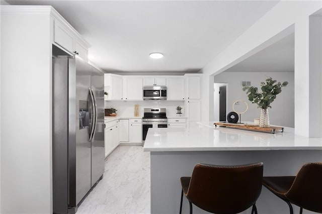 kitchen featuring white cabinetry, a kitchen breakfast bar, marble finish floor, appliances with stainless steel finishes, and light countertops