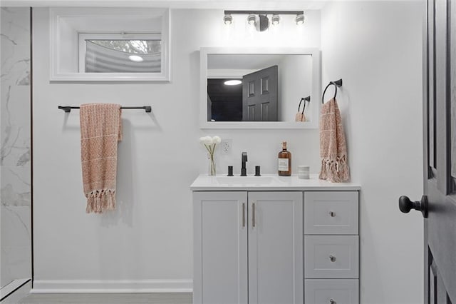 bathroom featuring baseboards, vanity, and a marble finish shower