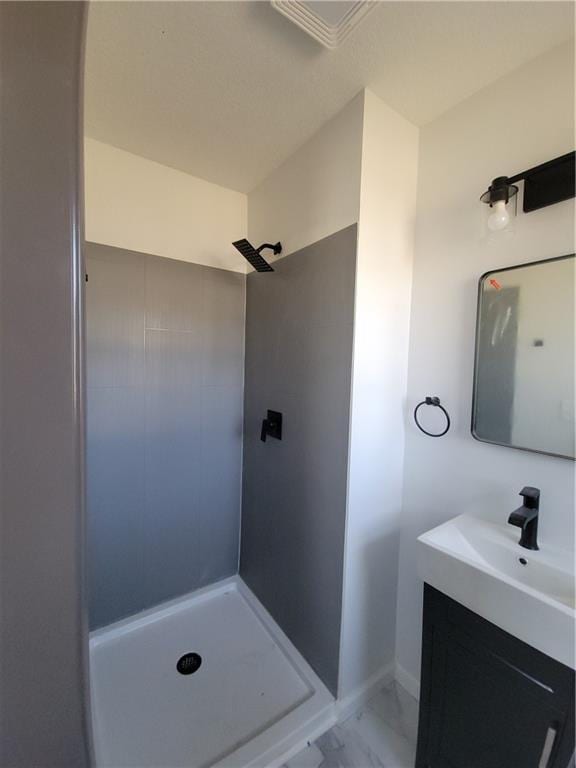 bathroom featuring vanity, baseboards, marble finish floor, and a tile shower