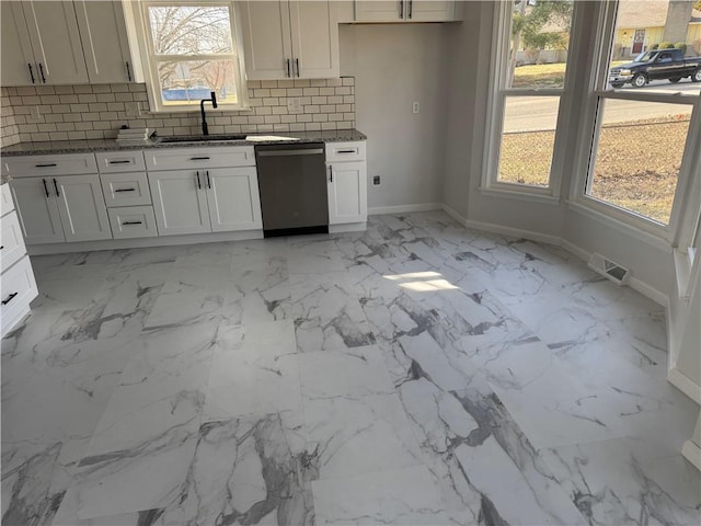 kitchen featuring backsplash, baseboards, dark stone countertops, stainless steel dishwasher, and a sink