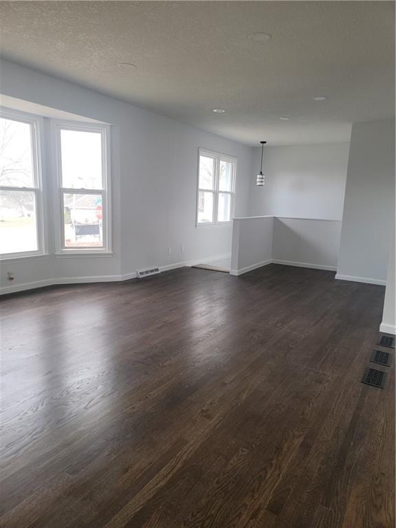 unfurnished living room with baseboards, visible vents, dark wood-style flooring, and a textured ceiling