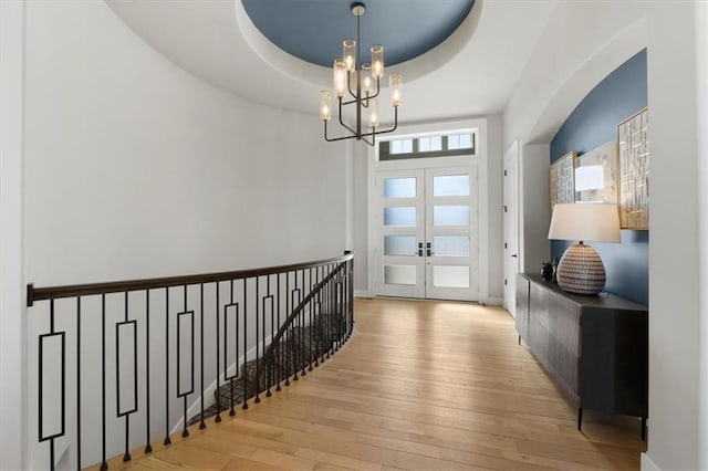 doorway with french doors, light wood-type flooring, a raised ceiling, and an inviting chandelier