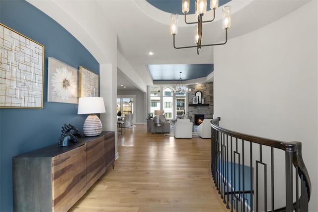 corridor with a tray ceiling, a notable chandelier, recessed lighting, and wood finished floors