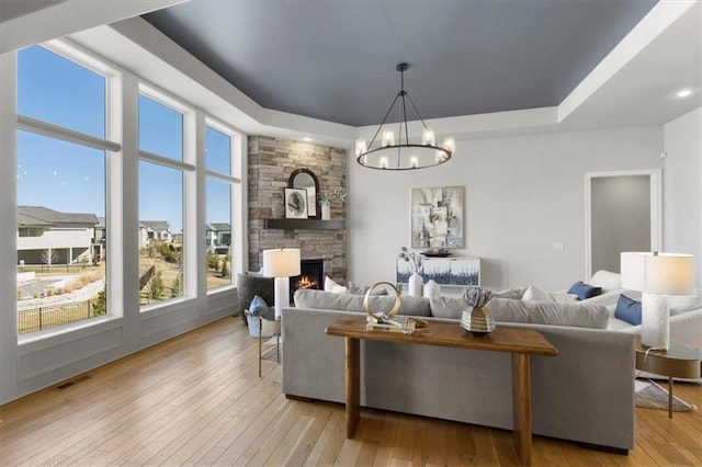 living area with a stone fireplace, a tray ceiling, light wood-style flooring, and a notable chandelier