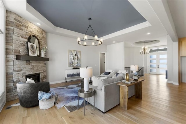 living room with a chandelier, a tray ceiling, a fireplace, and wood finished floors