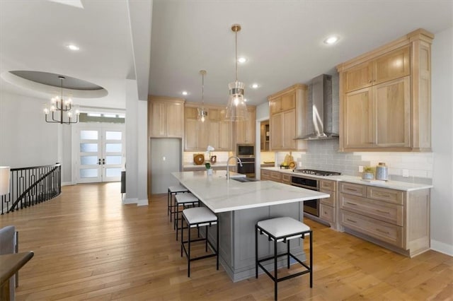 kitchen featuring light brown cabinets, light wood-style flooring, wall chimney range hood, appliances with stainless steel finishes, and a raised ceiling