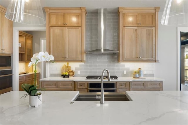 kitchen with stainless steel appliances, a sink, wall chimney range hood, and tasteful backsplash