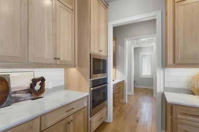 kitchen featuring appliances with stainless steel finishes, light stone countertops, light wood-type flooring, light brown cabinets, and backsplash