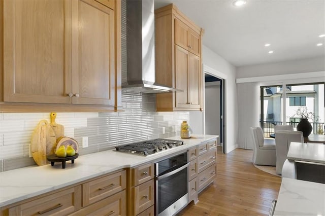 kitchen with stainless steel appliances, wall chimney range hood, light wood-type flooring, and light stone counters