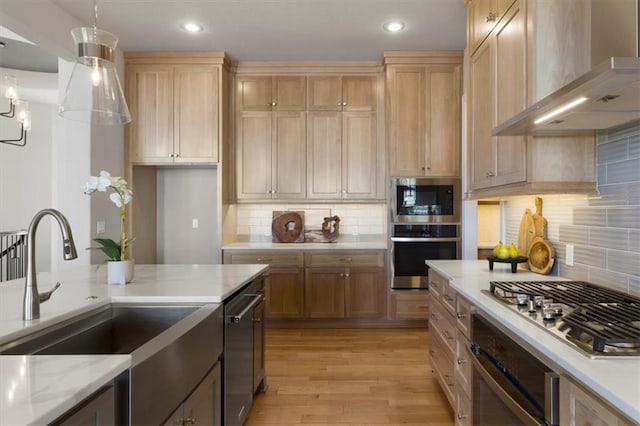 kitchen featuring stainless steel appliances, a sink, wall chimney range hood, light wood-type flooring, and light stone countertops