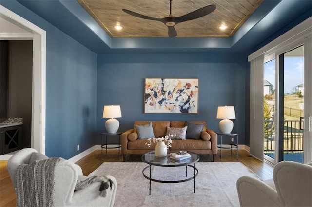 living area with baseboards, a ceiling fan, wood ceiling, wood finished floors, and a tray ceiling