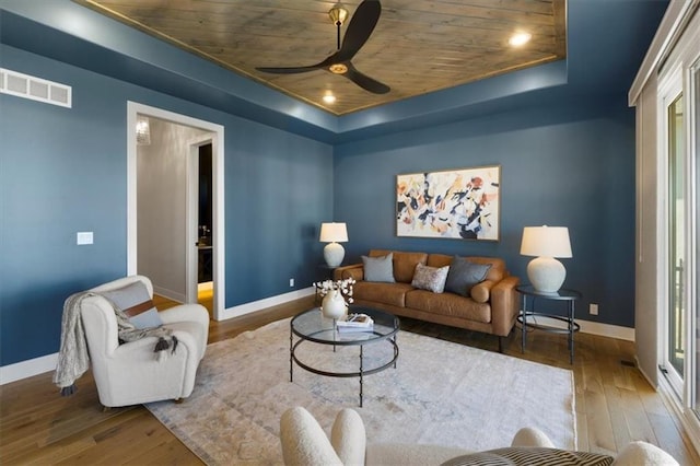 living area with a raised ceiling, visible vents, hardwood / wood-style floors, wooden ceiling, and baseboards