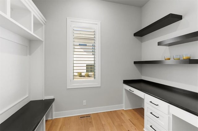 unfurnished office featuring light wood-type flooring, visible vents, built in desk, and baseboards