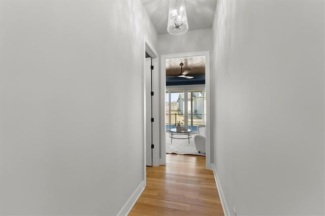 hallway featuring light wood-type flooring, baseboards, and an inviting chandelier